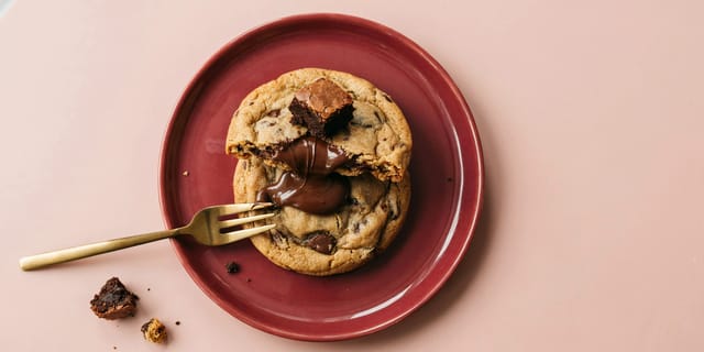 Aufgebrochener Schoko-Cookie mit flüssiger Schokolade auf einem weinroten Teller